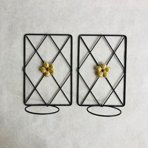 May include: Two black metal wall mounted candle holders with a gold flower design. Each holder has a circular base.