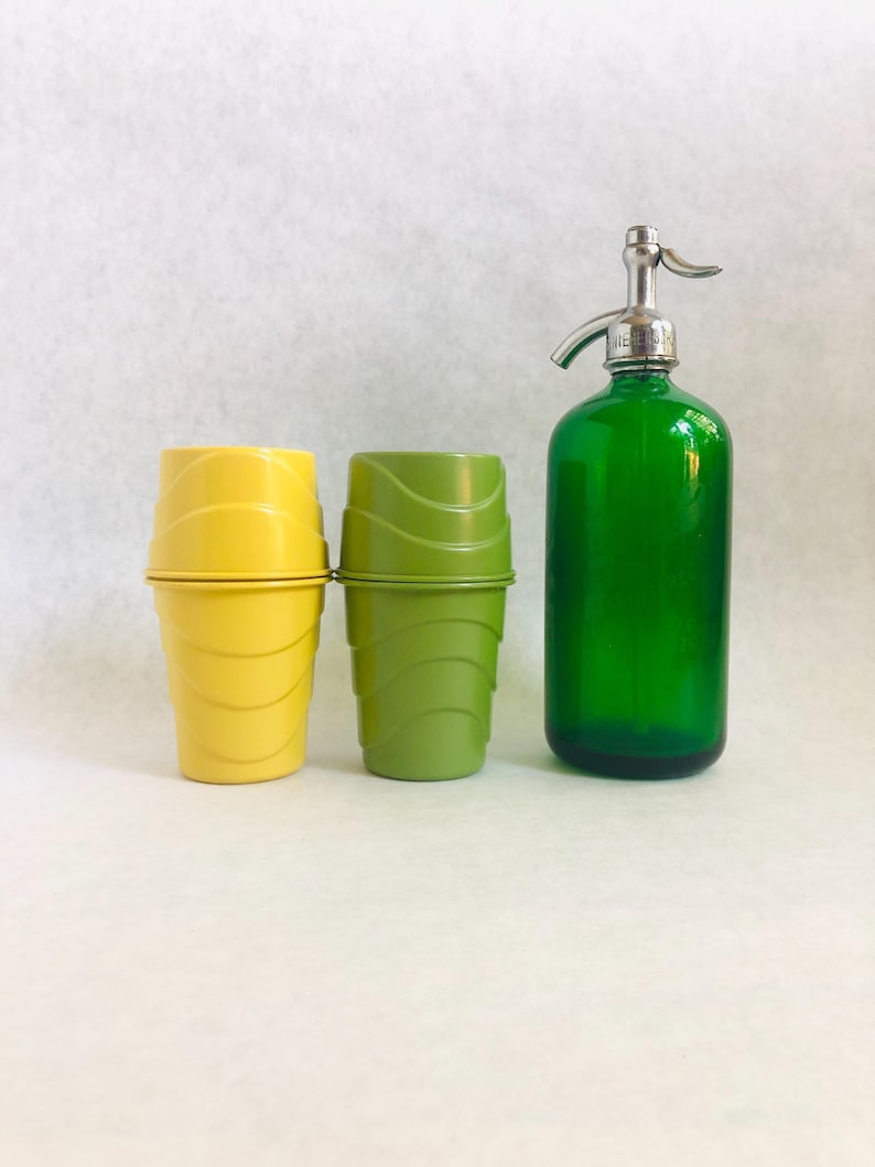 Puede incluir: Un juego de bar vintage con una botella de seltz de vidrio verde con una parte superior cromada y dos juegos de vasos de pl&aacute;stico amarillos y verdes. Las tazas tienen un dise&ntilde;o acanalado. La botella de seltz mide aproximadamente 30 cm de alto.