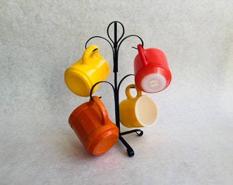 May include: A black metal mug rack with four mugs hanging from it. The mugs are yellow, orange, red, and white.