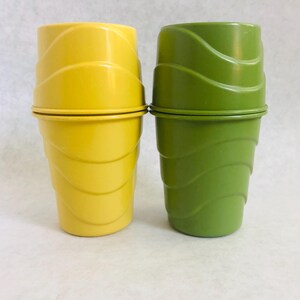 Puede incluir: Dos vasos apilables vintage, uno amarillo brillante y otro verde. Ambos tienen un dise&ntilde;o ondulado y acanalado, con una banda met&aacute;lica en el medio. Los vasos probablemente son de pl&aacute;stico.