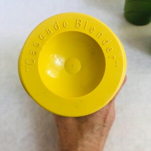 Puede incluir: Tapa de licuadora de color amarillo brillante, con las palabras "Cascade Blender" grabadas en el borde. La tapa es circular con un centro empotrado y est&aacute; sujeta por una mano.