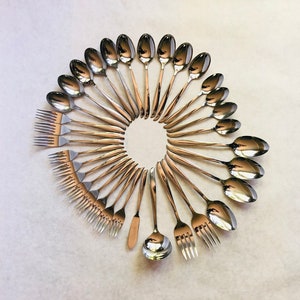 May include: A set of silver flatware arranged in a circle on a white surface. The set includes spoons, forks, and a butter knife.