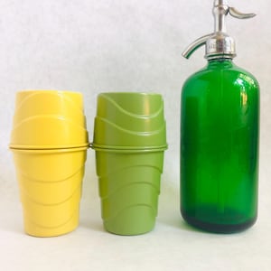 Puede incluir: Un vaso de helado amarillo y otro verde con tapas, junto a una botella de sif&oacute;n de vidrio verde con una boquilla plateada. Los vasos tienen un dise&ntilde;o acanalado. La botella de sif&oacute;n es de color verde vibrante.