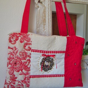 Peut inclure: Un sac fourre-tout en patchwork rouge et blanc avec un tissu floral, un tissu vichy rouge et un tissu rouge avec un petit portrait de femme dans un cadre doré. Le sac a des anses rouges et une fermeture éclair.