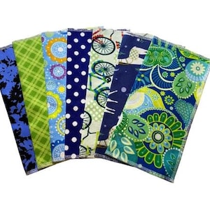 May include: A selection of seven patterned fabric napkins. Designs include floral, polka dots, bicycle, and paisley prints in blue, green, and yellow. Each napkin has a stitched edge. The napkins are arranged in a fan shape.