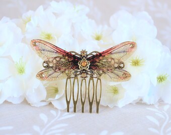 May include: A gold butterfly hair comb with translucent wings decorated with glitter and a small orange gem in the centre. The wings are a gradient of pink and brown.