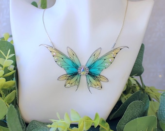 May include: A silver chain necklace featuring a blue and yellow butterfly pendant. The butterfly has iridescent wings and a clear crystal at its centre.