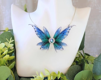 May include: A silver chain necklace with a blue and green iridescent butterfly pendant. The butterfly has a clear crystal in the centre.