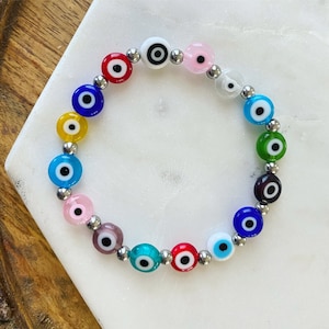 May include: A colorful evil eye bracelet with silver beads. The bracelet features a variety of colors, including red, blue, green, yellow, and pink.