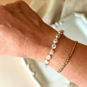 Puede incluir: Un brazalete de cadena dorada con un brazalete de abalorios con peque&ntilde;as cuentas de ojo turco blancas y azules.