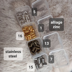 Peut inclure: Divers ressorts hélicoïdaux métalliques dans des boîtes en plastique transparent. Les ressorts sont de différentes couleurs, dont argent, or et bronze. Le texte "stainless steel" et "alliage zinc" est visible.