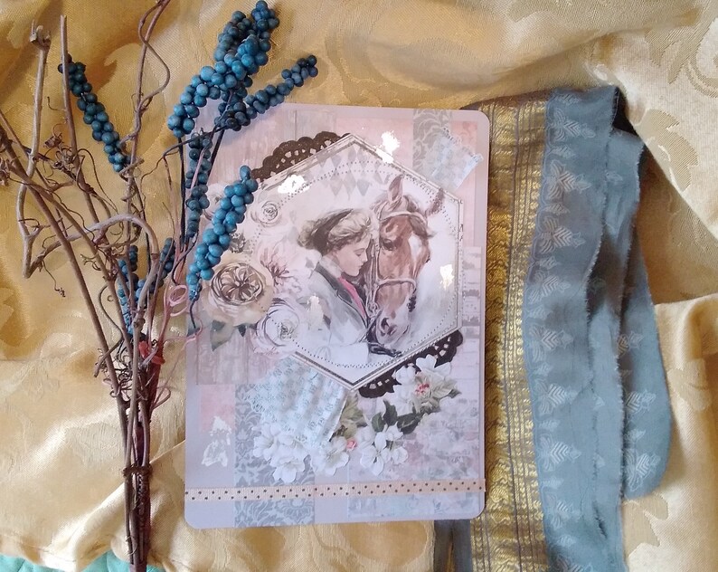 Puede incluir: Una tarjeta decorativa de estilo vintage con una ilustraci&oacute;n de una mujer y un caballo. La tarjeta tiene un marco hexagonal y est&aacute; adornada con motivos florales y de encaje. Tambi&eacute;n hay una ramita de bayas azules y una cinta azul.