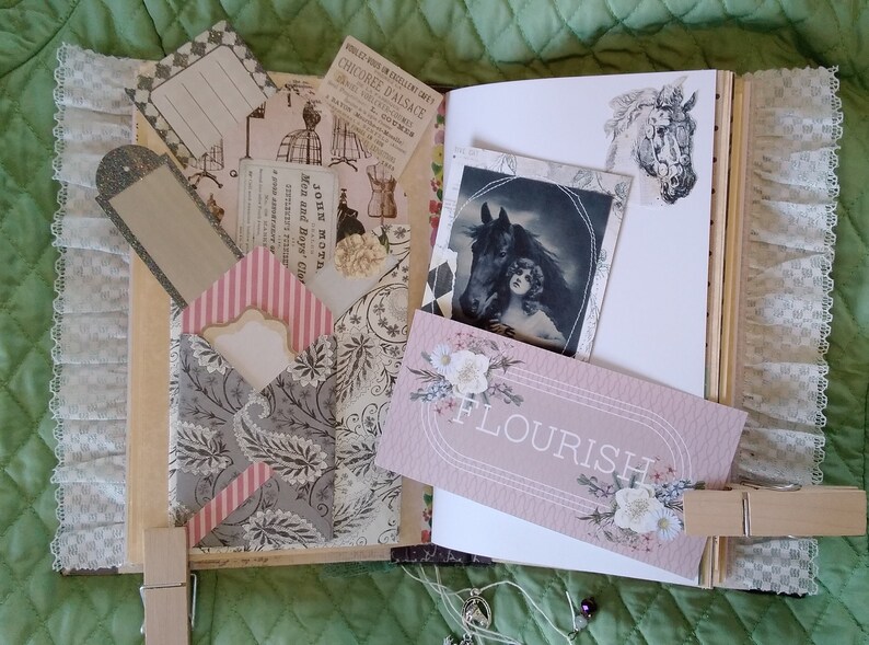 Puede incluir: Un diario hecho a mano con papel decorativo, ribete de encaje y ef&iacute;meras vintage. El diario presenta una tarjeta rosa con la palabra "FLOURISH" y una imagen en blanco y negro de una mujer y un caballo. El diario se cierra con una pinza de madera.