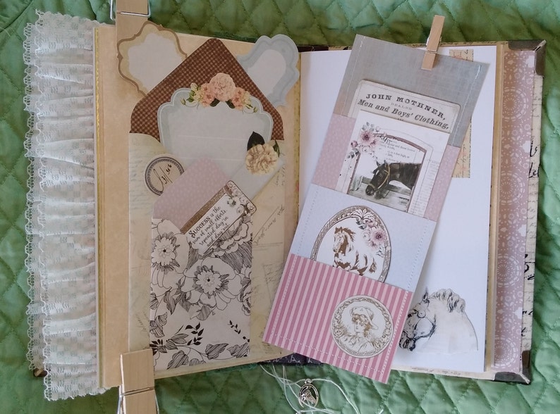 Puede incluir: Diario abierto con p&aacute;ginas decorativas, bolsillos y adornos. Presenta dise&ntilde;os florales y de estilo vintage, incluyendo un bolsillo con una ilustraci&oacute;n de caballo y el texto "JOHN MOTHNER, Men and Boys' Clothing." Incluye ribete de encaje y etiquetas de papel.