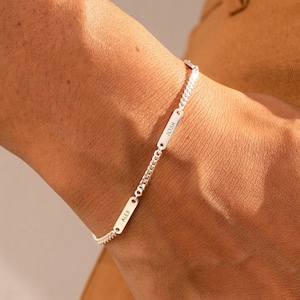 May include: A silver chain bracelet with small rectangular charms. The charms have engraved text on them.