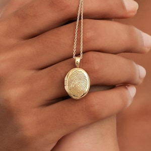 May include: A gold necklace with a locket pendant featuring a detailed fingerprint design.