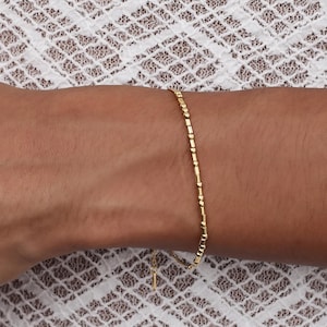 May include: A delicate gold bracelet with small, round beads. The bracelet is shown on a person's wrist.