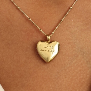 May include: A gold chain necklace with a heart-shaped locket. The locket has the words "Love amore" engraved on it.