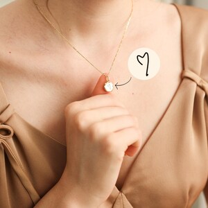 May include: A gold necklace featuring a small, round, polished pendant with a delicate, hand-drawn heart symbol engraved on its surface. The pendant hangs from a thin, matching gold chain, showcasing a minimalist design with a clear, dark heart icon.