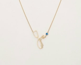 May include: A gold-colored necklace featuring a stethoscope design with the name "Jennifer" in cursive script. The necklace includes a blue and a yellow gemstone, and is a medical-themed jewelry piece.
