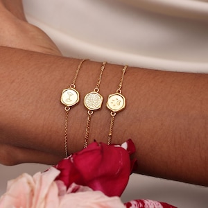 May include: Three gold-toned chain bracelets featuring small hexagonal charms. The first charm displays a line drawing of a shell, the second has a textured dotted surface, and the third charm features an engraved paw print design.