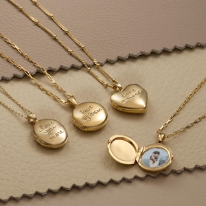 May include: Gold locket necklaces with fine chains. The lockets are in oval and heart shapes, with engraved phrases such as "Love you more" and "You're my Person." One locket is open, displaying a small photograph. The chains are approximately 40-50 cm long.