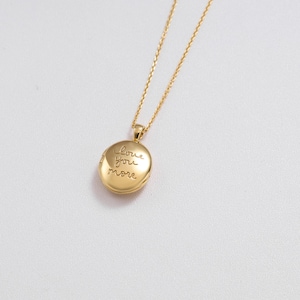 May include: A gold-colored, round pendant necklace with the inscription "love you more." The pendant hangs from a delicate gold chain. The necklace is set against a white background, highlighting the jewelry's design.