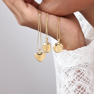 May include: Three gold-colored necklaces with cross pendants. One pendant is heart-shaped, while the other two are round. The necklaces are displayed against a white background, showcasing the jewelry's design and color.