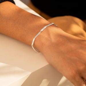 May include: A silver-toned chain bracelet featuring two small, rectangular metal plaques. Each plaque is engraved with a name, specifically Alex and Josh, integrated into the delicate link chain design that encircles the wrist.