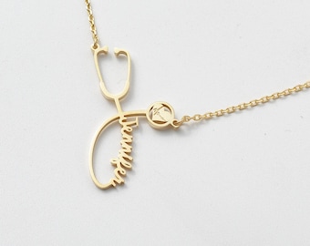 May include: A gold-toned necklace featuring a pendant shaped like a stethoscope. The name Jennifer is written in cursive script along the tubing of the stethoscope, and a small circular charm with a heart-shaped EKG line is attached to the side.