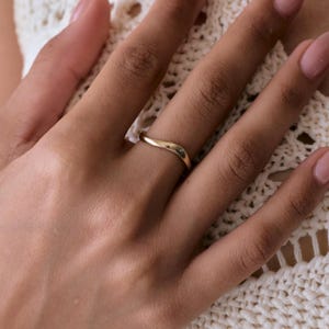 May include: A polished gold ring featuring a smooth, continuous wave-like design. The band has a rounded profile and a reflective metallic finish, creating a gentle curve that sits evenly around the finger without any additional stones or engravings.