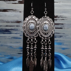 May include: Silver dangle earrings with a white stone center and feather accents.
