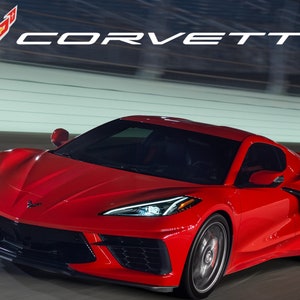 May include: A red Chevrolet Corvette sports car driving on a race track at night. The car has a black front bumper and black wheels. The Corvette logo is visible on the front of the car.
