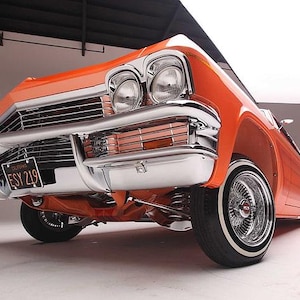 Könnte beinhalten: Niedrige Winkelaufnahme eines klassischen orangefarbenen Autos mit Chromakzenten. Das Auto hat ein Nummernschild mit der Aufschrift "ESY 219". Die Reifen haben weiße Seitenwände. Das Auto befindet sich in einem Studio.