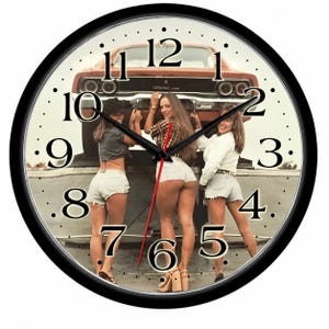 May include: A round wall clock with a black frame and a white face featuring black numbers. The background image shows three individuals standing in front of a vintage orange car, wearing casual tops and light-colored denim shorts. Black hour and minute hands and a red second hand are centered on the clock face.
