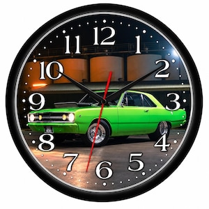 May include: A round wall clock with a black frame and a white face featuring large black numbers. The center image displays a bright green vintage muscle car parked in front of industrial tanks at night. It has black hour and minute hands.