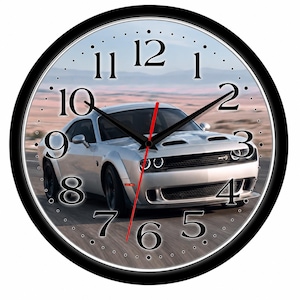 May include: A round wall clock with a black frame featuring a silver Dodge Challenger SRT car on the face. The clock has black hour and minute hands, a red second hand, and large black serif numerals from 1 to 12 against a desert road background.