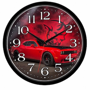 May include: A round wall clock with a black frame and a red and black background featuring a red muscle car and a demon logo. The clock face displays white Arabic numerals from 1 to 12, with black hour and minute hands and a thin red second hand.