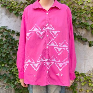 May include: A pink long-sleeved button-up shirt with a white geometric pattern.