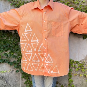 May include: A long-sleeved, orange button-down shirt with a white geometric pattern of triangles on the left side.