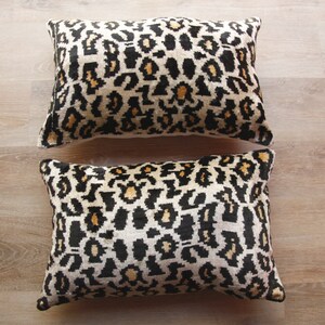 May include: Two decorative throw pillows with a leopard print pattern. The pillows are made of a soft, plush fabric and feature a black, white, and gold color scheme.