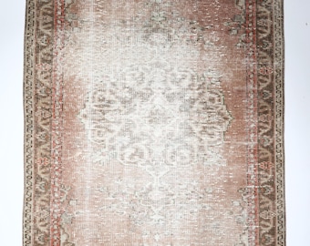 May include: A rectangular, distressed-look rug with a central medallion design. The rug features a faded color palette of dusty rose, cream, and brown, with a detailed border. The rug's design suggests a vintage or antique style, suitable for home decor.