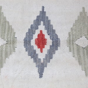 May include: A white woven rug with a repeating pattern of gray, blue, and red diamond shapes.