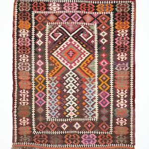 May include: A traditional Turkish rug with a dark red background and intricate geometric patterns in shades of pink, orange, blue, and green. The rug has a fringe border.