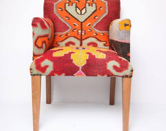 May include: A decorative armchair with a vibrant, patterned textile design. The chair features a red background with orange, yellow, and green geometric shapes. The wooden legs provide a natural contrast to the colorful upholstery.