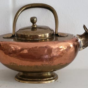 May include: A vintage copper and brass teapot with a unique animal-shaped spout. The teapot has a rounded body and a lid with a knob. The spout is shaped like a bull's head.