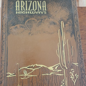 Puede incluir: Portada de libro vintage de "Arizona Highways" en tonos marrón y dorado. La portada presenta ilustraciones estilizadas de cactus y paisajes desérticos. El título se muestra prominentemente en letras doradas.