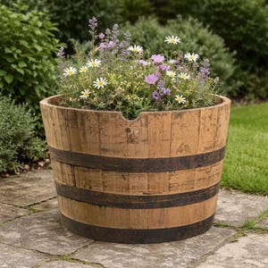 May include: A large, round wooden planter filled with a variety of colorful flowers. The planter is made of weathered wood with dark metal bands. The flowers include white daisies, purple blooms, and lavender.