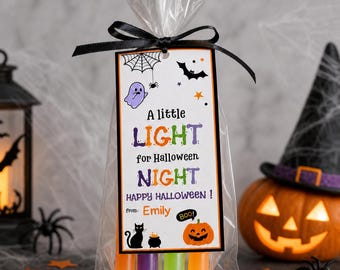 May include: A clear plastic treat bag tied with a black ribbon and a rectangular tag featuring the text A little LIGHT for Halloween NIGHT HAPPY HALLOWEEN! from: Emily BOO! with illustrations of a ghost, spider web, bat, cat, and pumpkin.