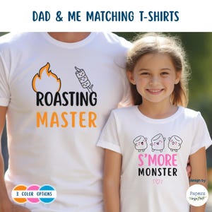 Puede incluir: Camisetas blancas con diseños a juego. Una camiseta dice "ROASTING MASTER" con un gráfico de llama y malvavisco. La otra dice "S'MORE MONSTER" con personajes de malvavisco. El texto "DAD & ME MATCHING T-SHIRTS" está en la parte superior.